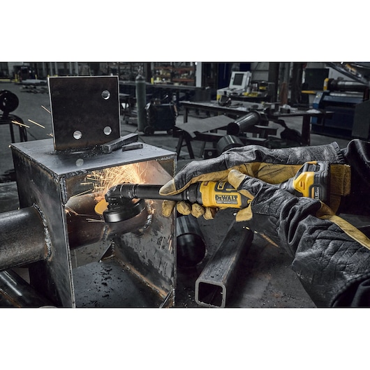 A person wearing protective gloves uses a yellow DEWALT cordless grinder to smooth the inside of a metal structure, producing sparks in an industrial workshop setting.
