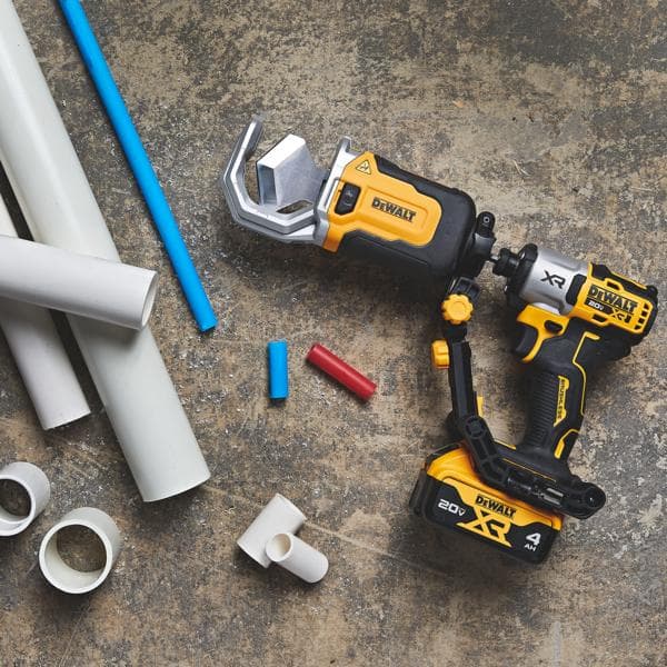 A DEWALT cordless power tool designed for cutting PVC pipes, shown on a concrete surface beside several white and colored pipes and pipe fittings.