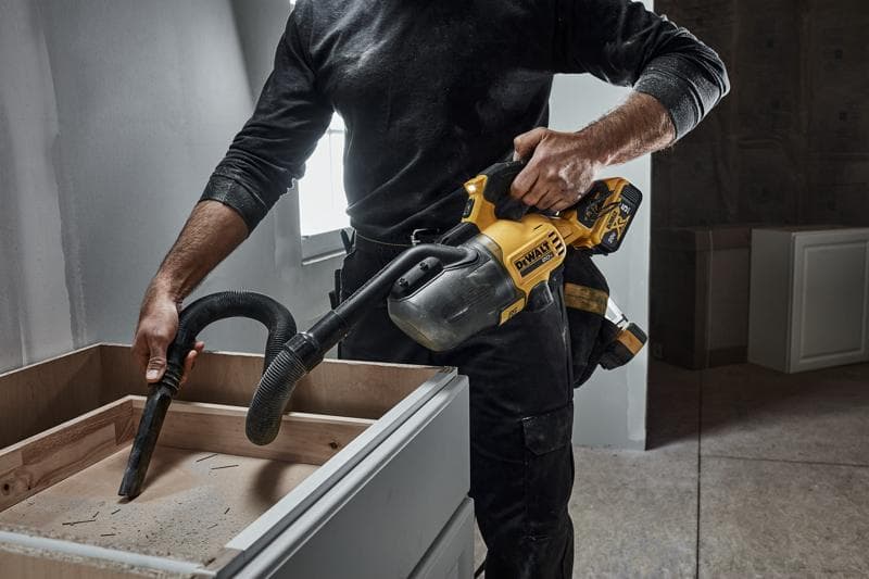 A person using a DEWALT cordless portable vacuum to clean sawdust from a cabinet drawer in a workshop or construction setting.