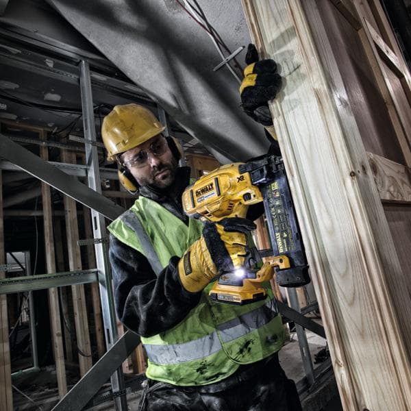 Worker uses DEWALT DCN680 nailer on wooden frame at construction site, wearing safety gear and gloves.