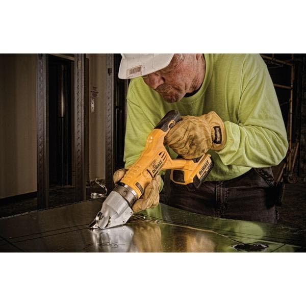 A worker wearing a hard hat and gloves uses a yellow DEWALT cordless metal shear tool to cut sheet metal.