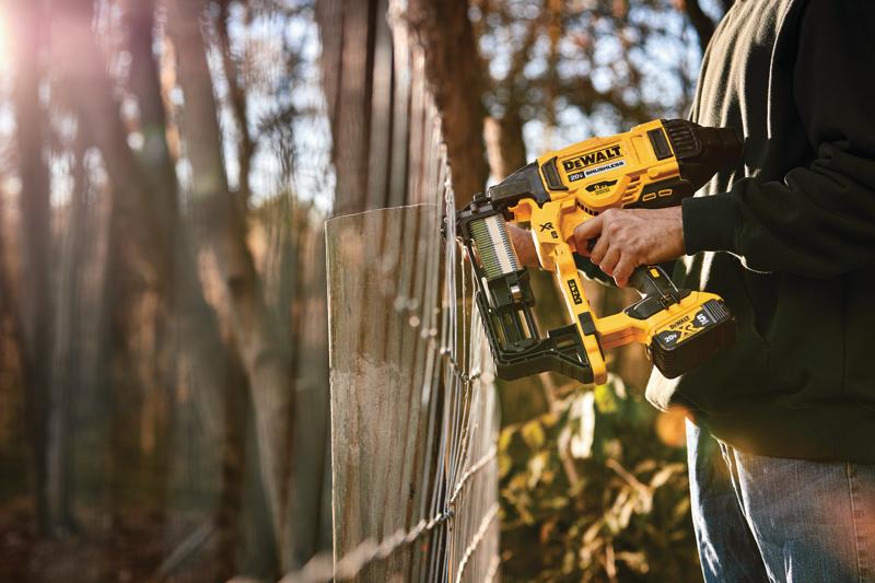 A person using a DEWALT cordless fencing stapler to secure wire fencing outdoors, with trees and sunlight in the background.