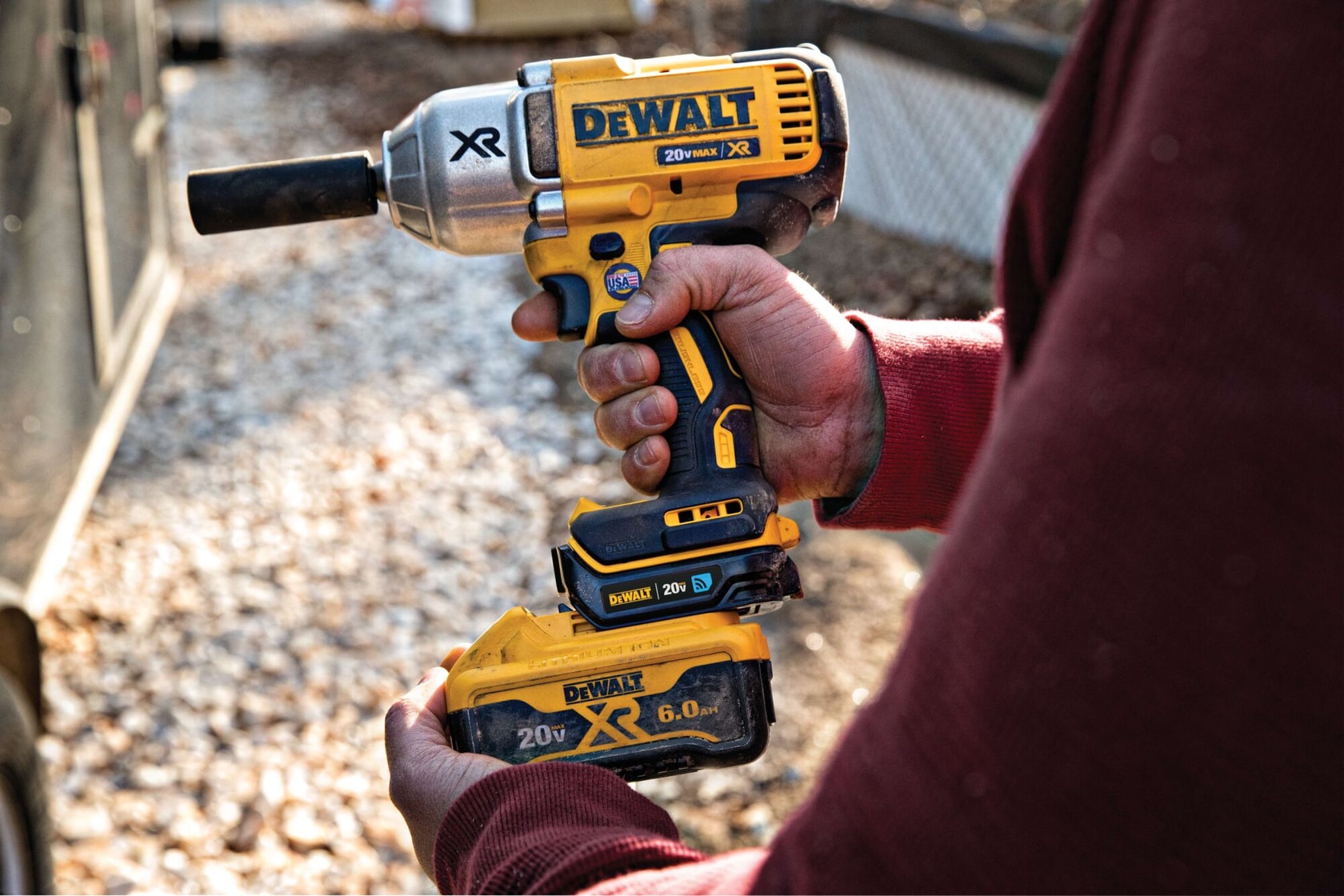 A person holding a DEWALT 20V Max XR cordless impact wrench with a yellow battery outdoors, with a blurred background.