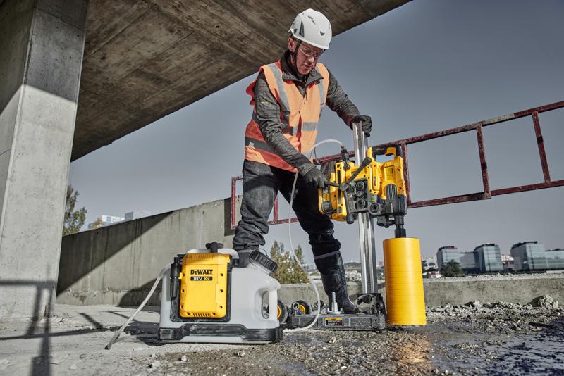 Worker uses DEWALT DCPS151 core drill on concrete at construction site, wearing safety helmet and vest.