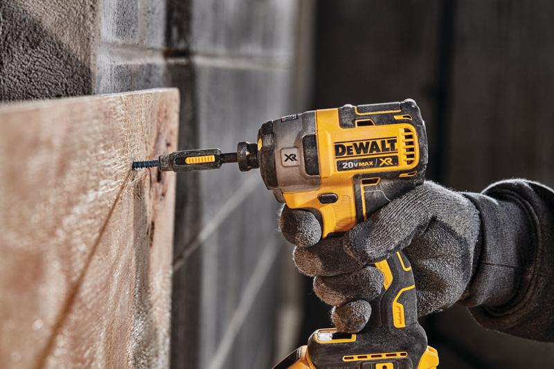 A person wearing work gloves uses a yellow and black DEWALT 20V MAX XR cordless impact driver to drive a screw into a wooden board.